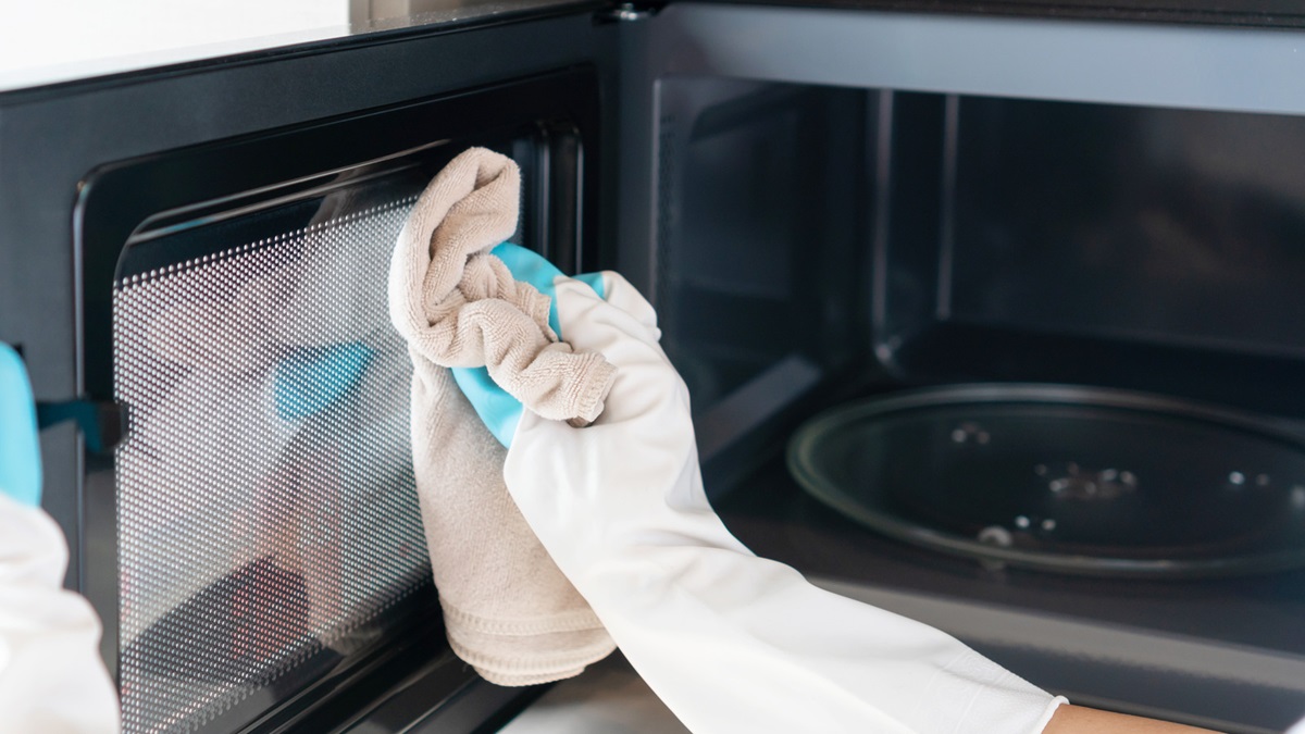 Woman hand with microfiber rag cleaning inside of microwave oven. Closeup